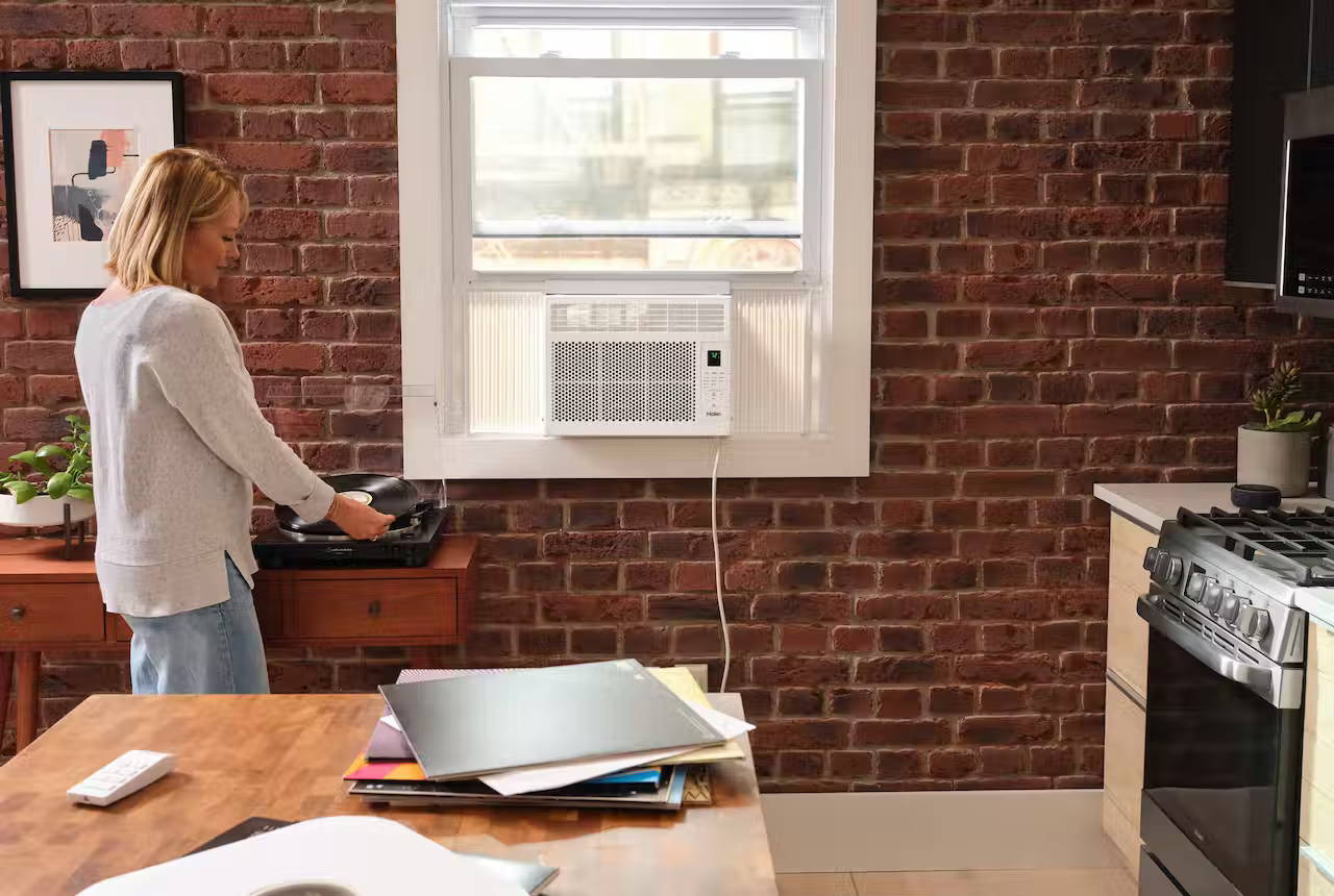 Woman plays records on a turntable next to the kitchen window with a Haier window air conditioner.