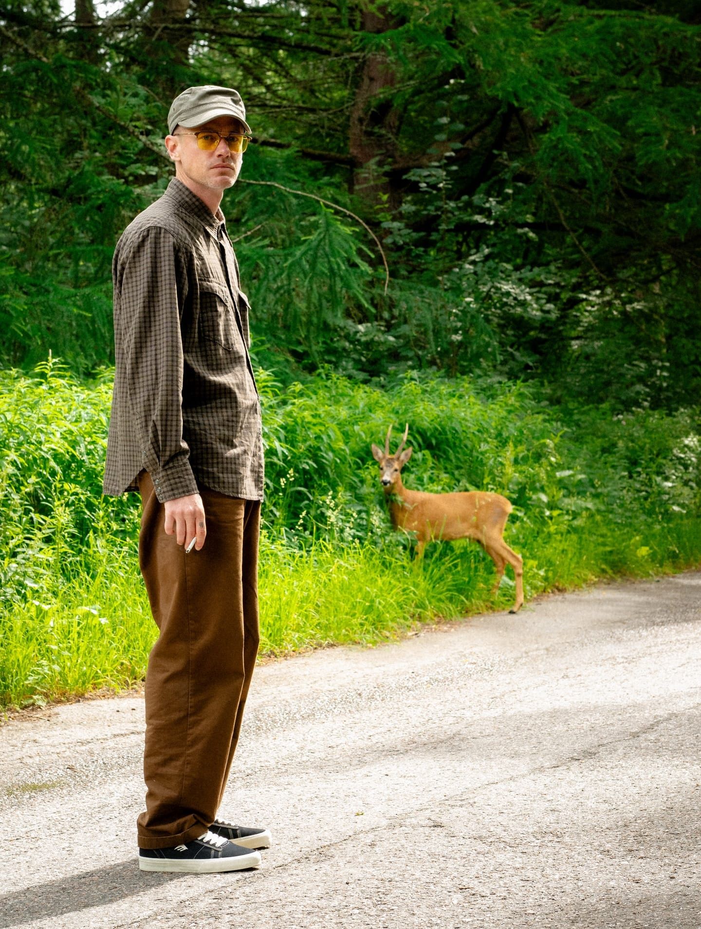 Person standing on a road with a deer in the background.