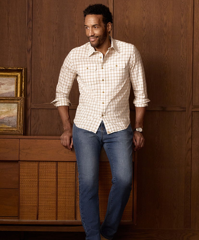 Man standing next to a wooden cabinet, wearing a checked shirt and jeans.