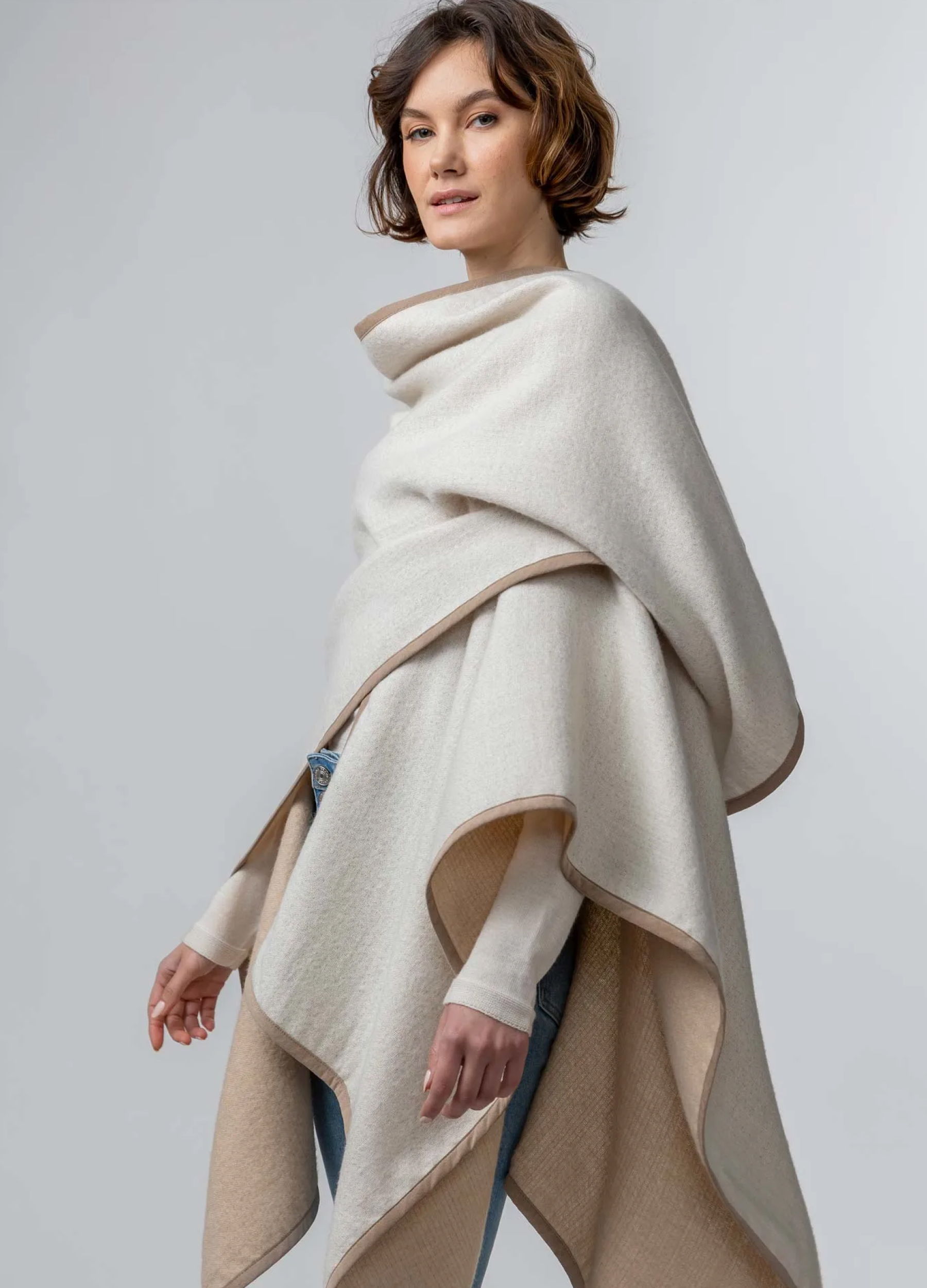 Woman wearing a stylish beige poncho against a neutral background.