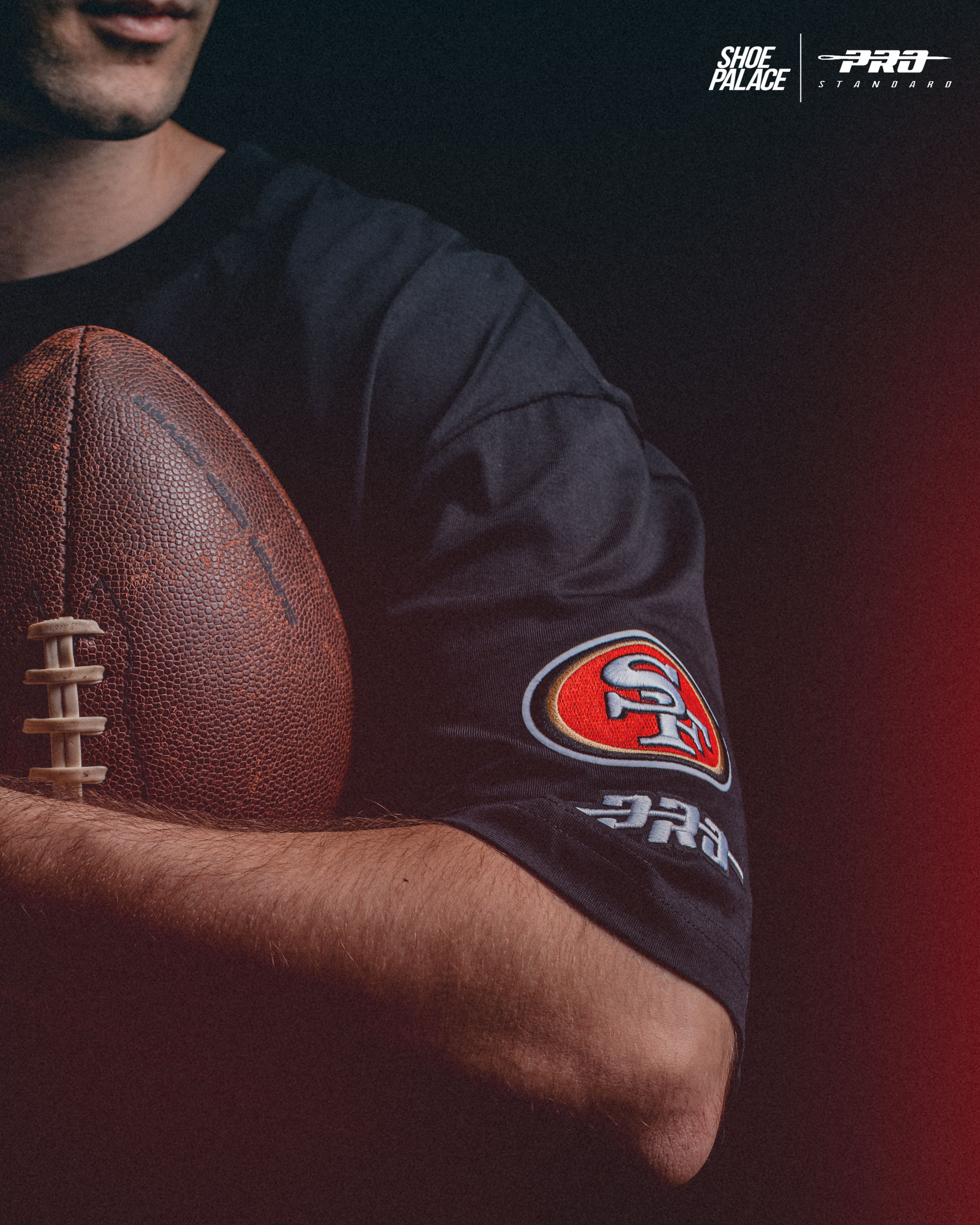 Person holding a football, wearing a black shirt with a logo.