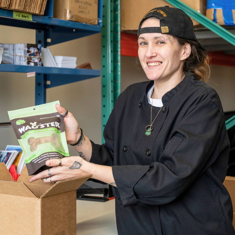 Person in a black chef's jacket holding a product package in a warehouse.