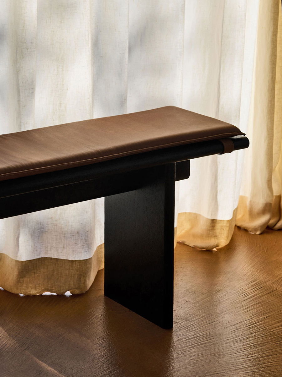 A modern &tradition bench near sheer curtains on a wooden floor.
