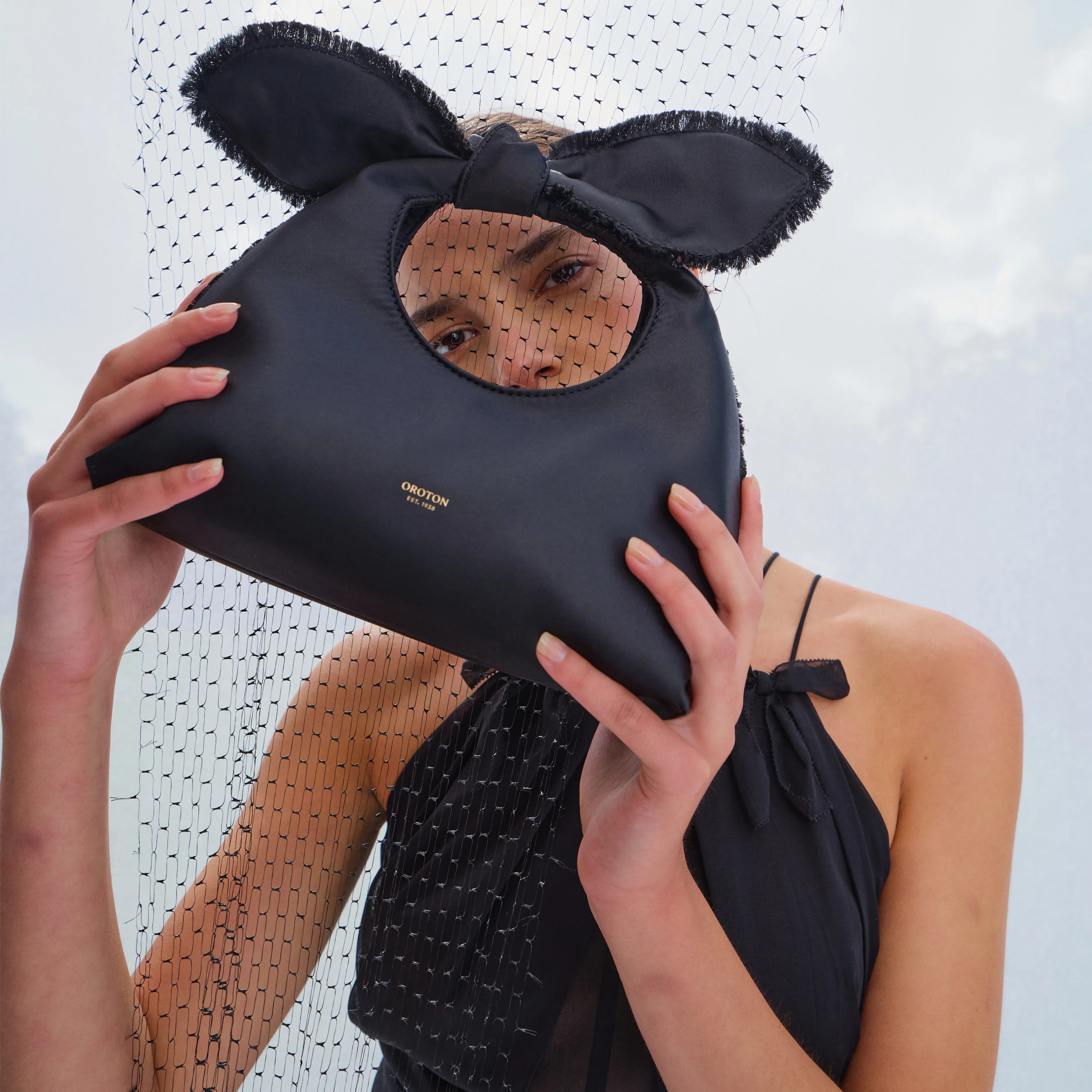 Person holding a unique black handbag with ear-like features against a sheer backdrop.