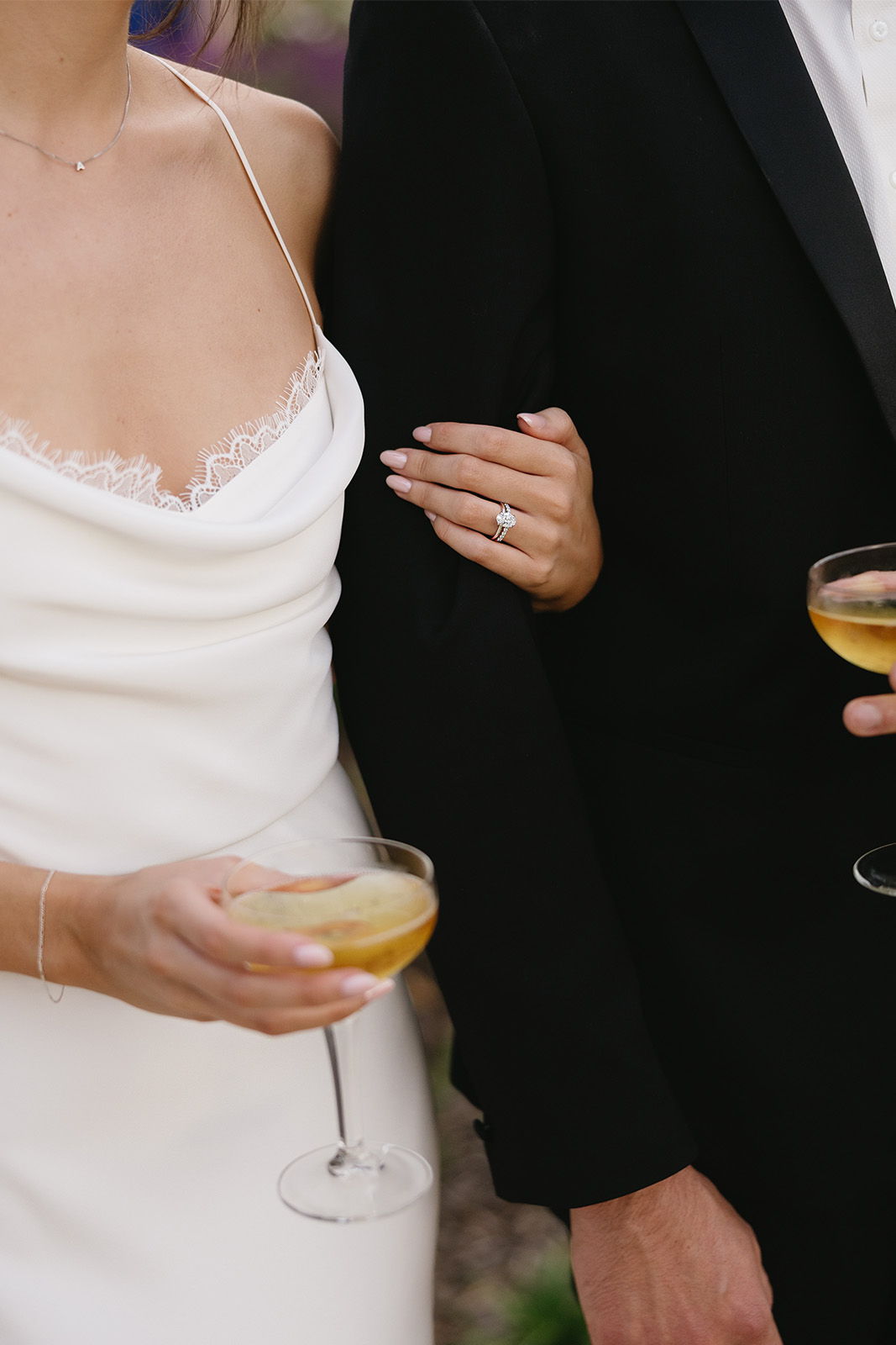Bride and groom holding champagne glasses, with a close-up on their hands.