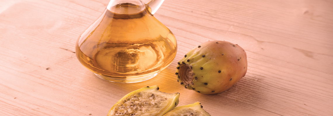 A glass oil container next to sliced fruit on a wooden surface.