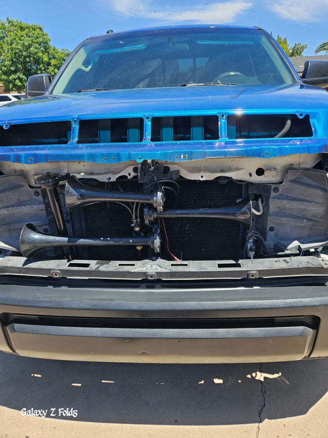 Front close-up metallic blue Tundra grille removed four black train horns mounted in front of radiator solenoid wiring Brian's Conductor's Special 228H install gallery photo 2