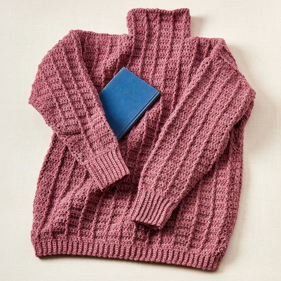 A mauve knitted sweater with a blue book placed on it.