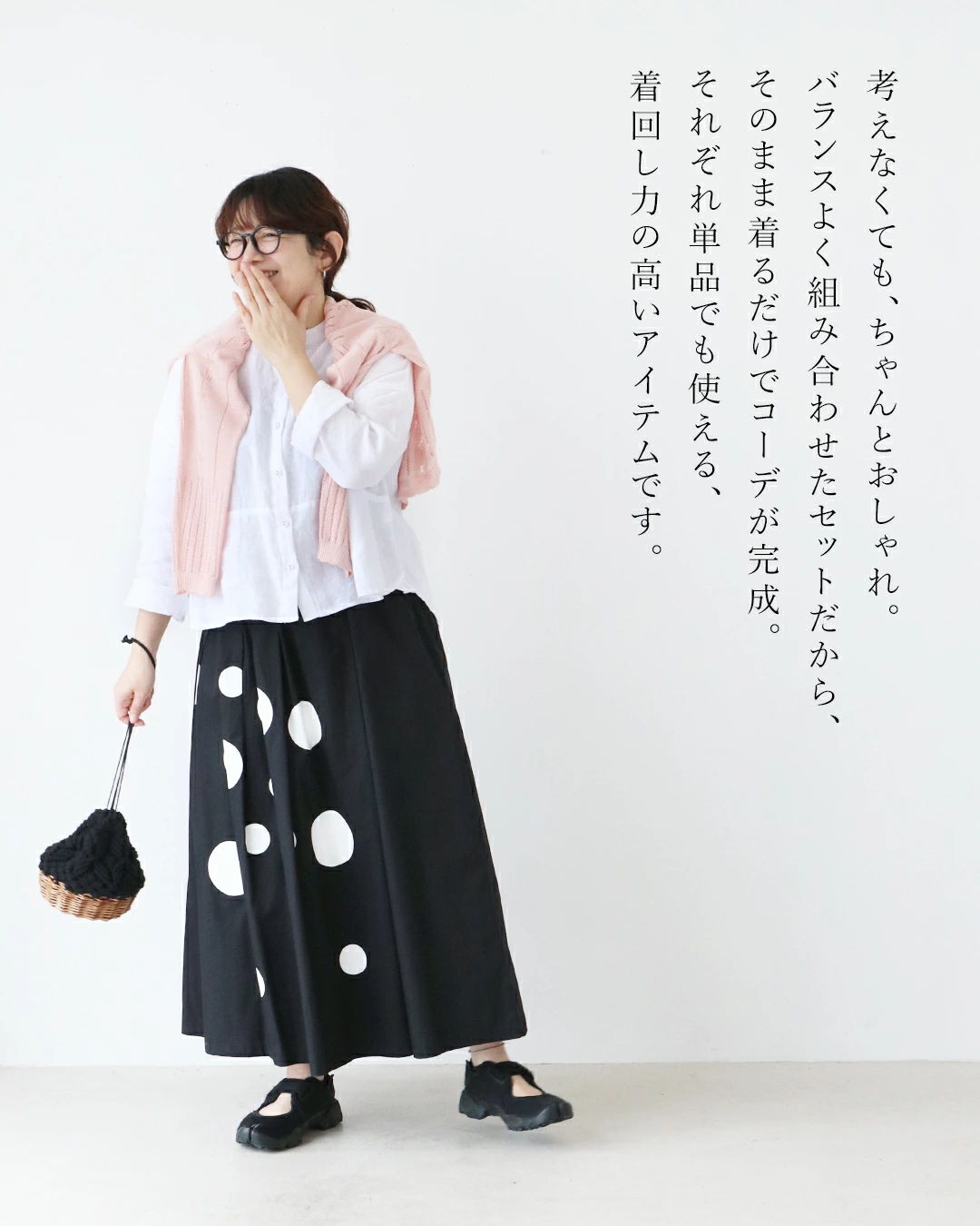 Woman in polka dot skirt and pink cardigan, holding a bag.