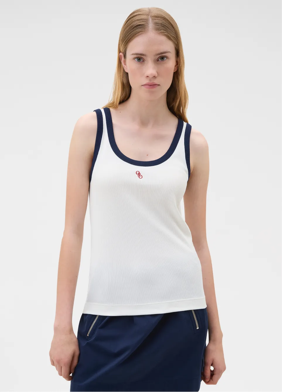 Woman wearing a white tank top with navy accents and a small logo.