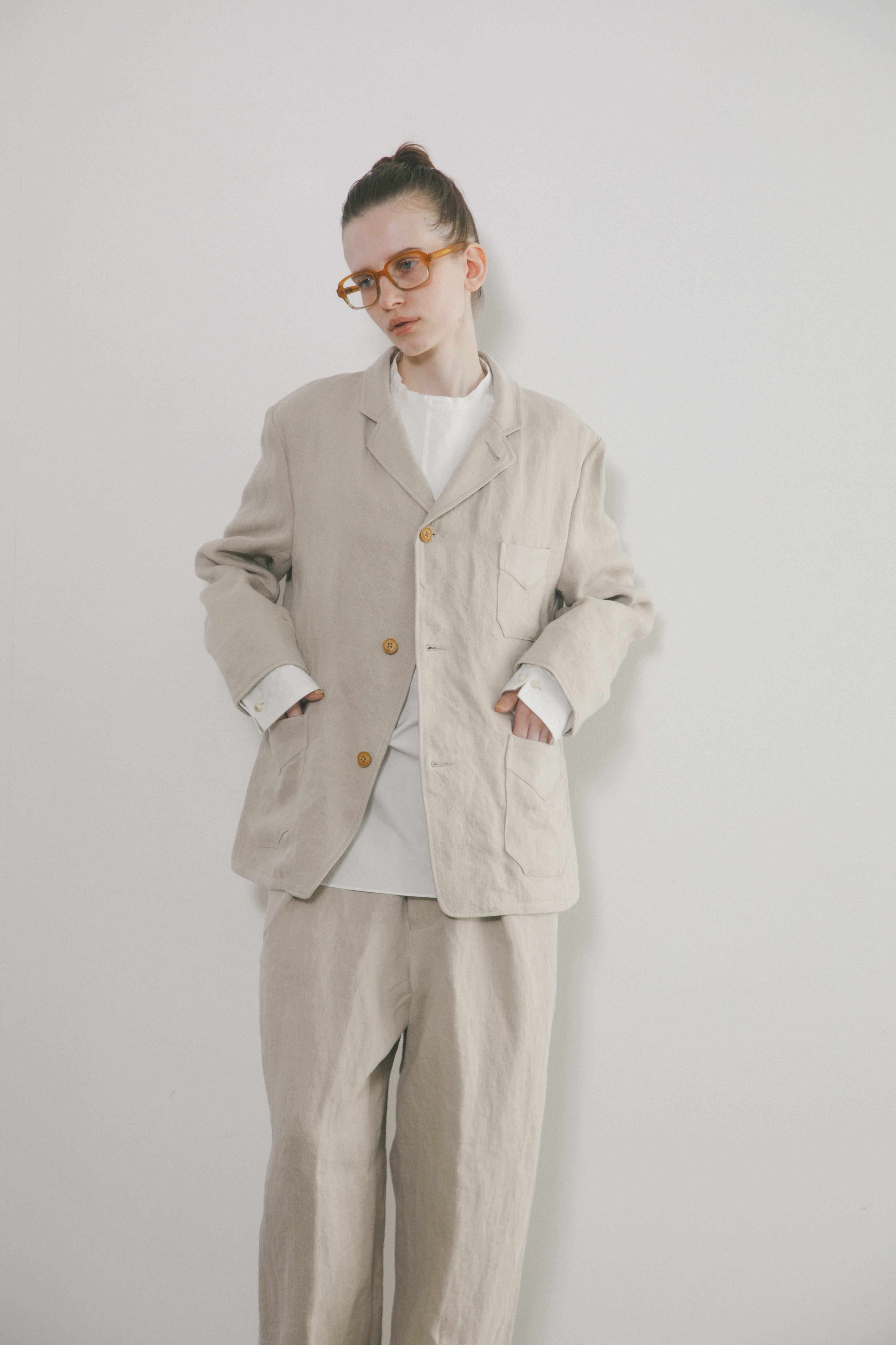 A person wearing a beige suit with glasses, standing against a white background.