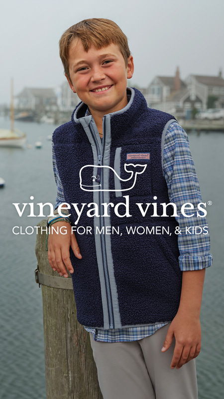 Boy in a vest smiles by the water, vineyard vines logo included.