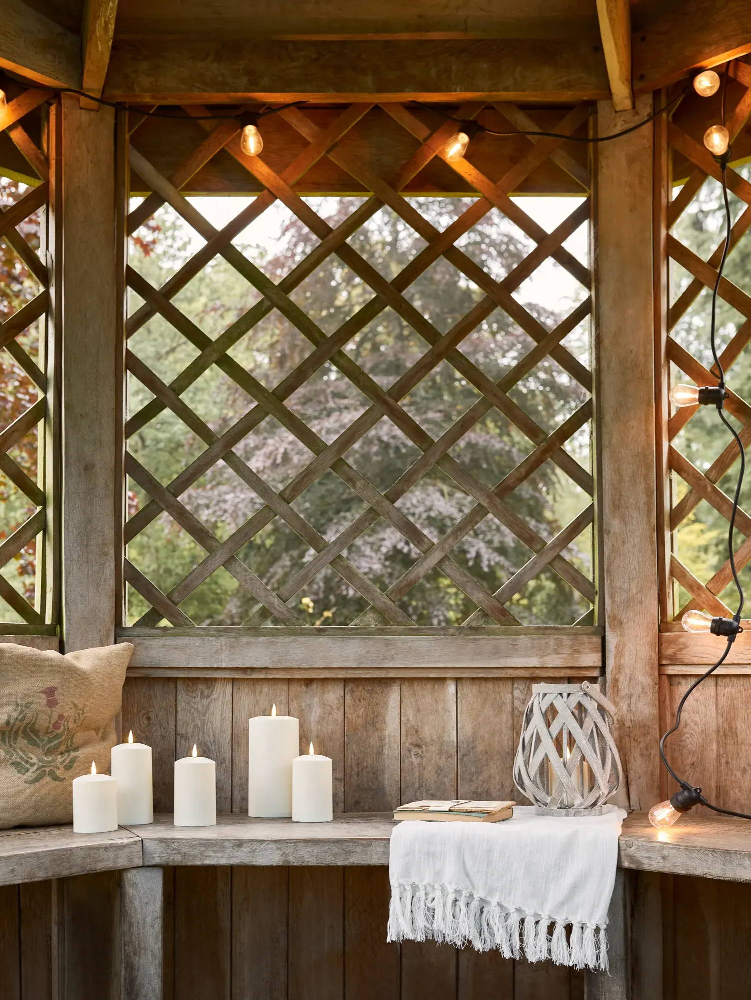 Outdoor summerhouse setting with festoons hung from roof and TruGlow candles sat on bench
