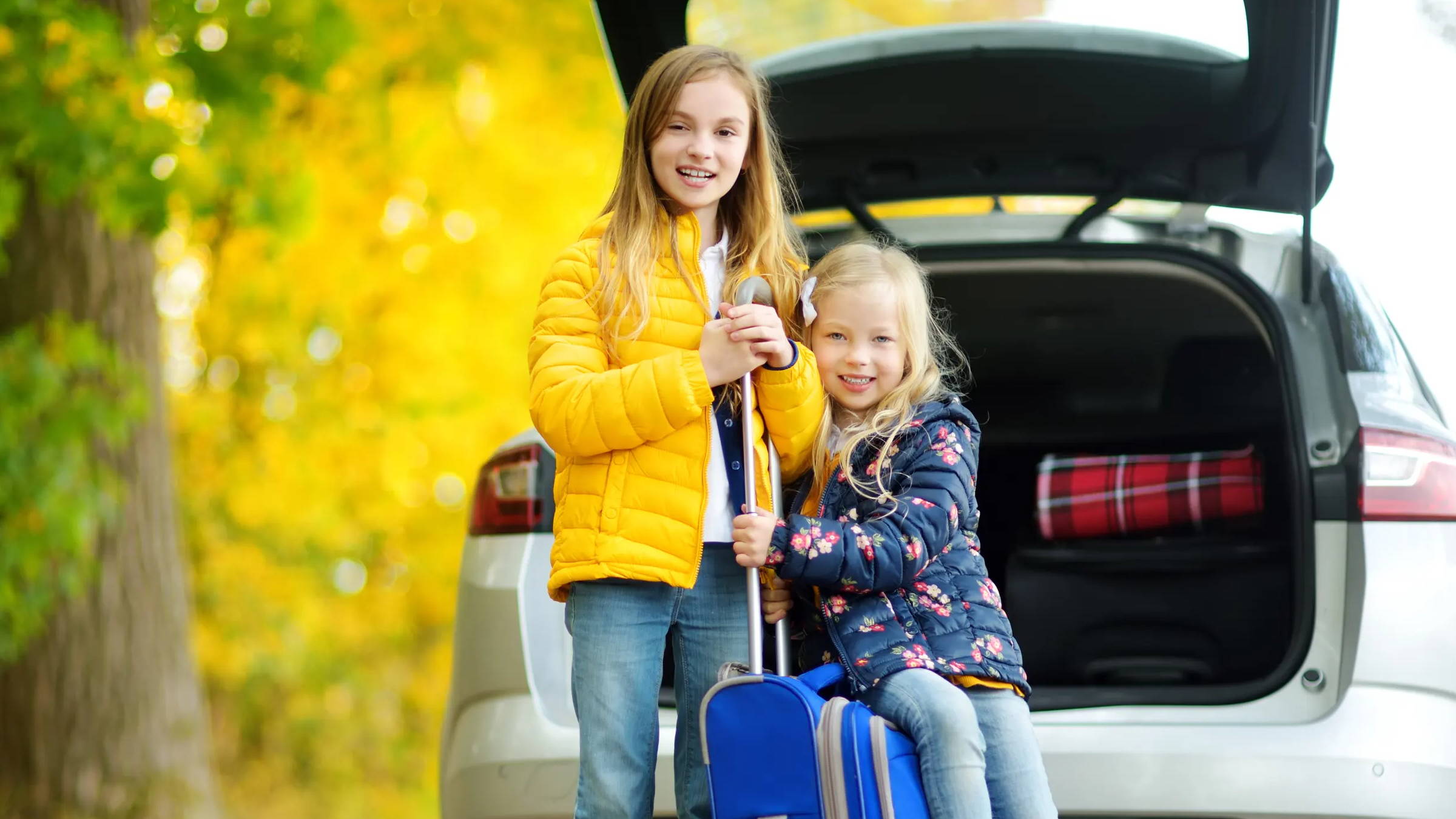 Kids holding luggage outside of car in the fall