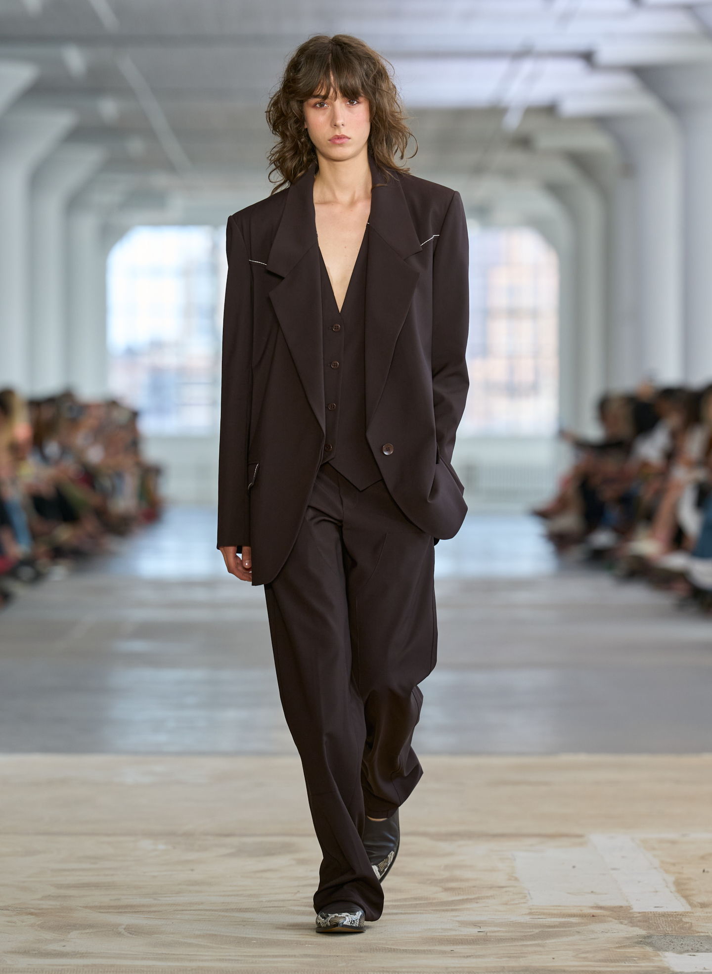 Model walking down runway in oversized black suit.