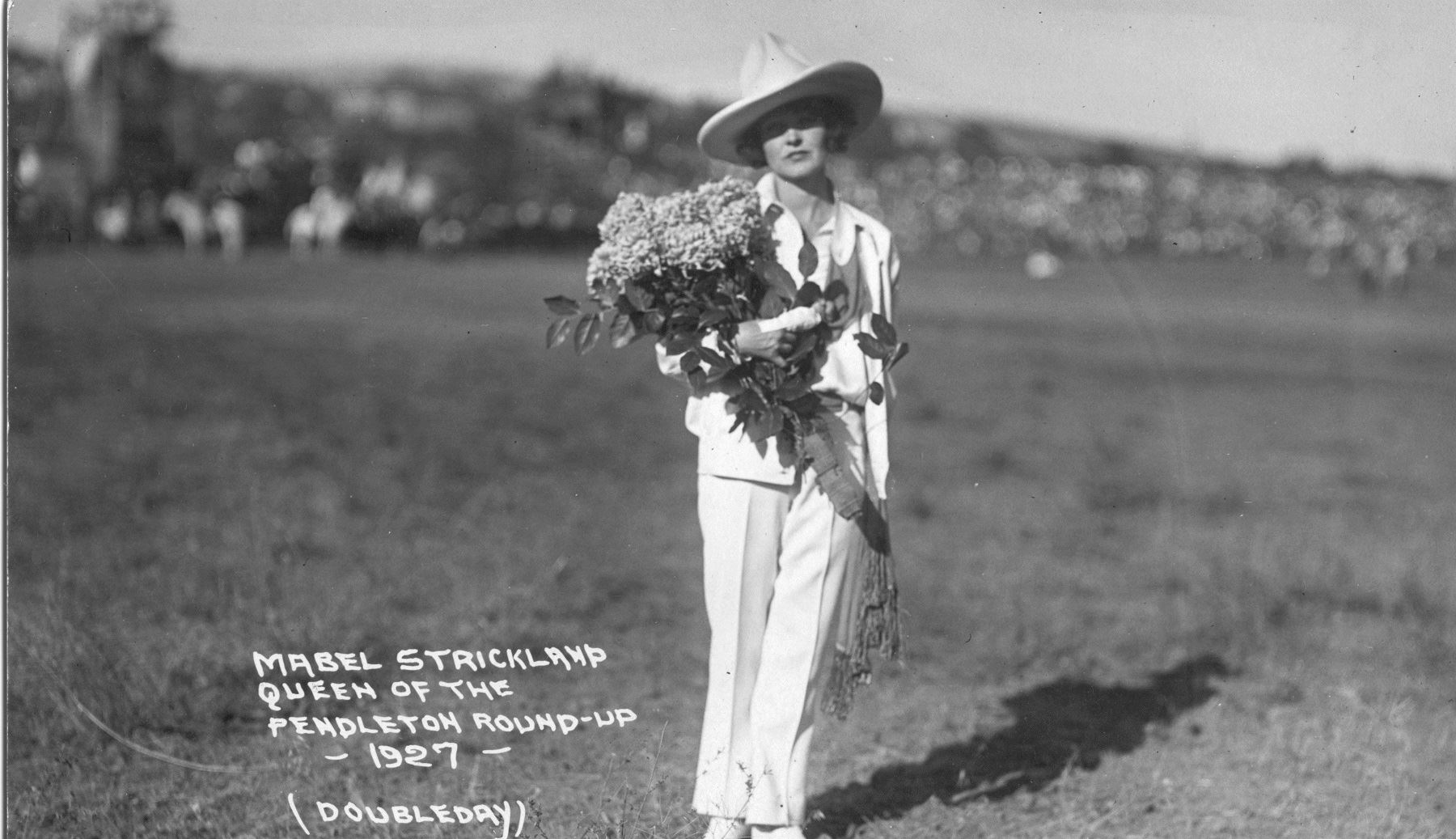 A woman in a white suit holding flowers in a field.