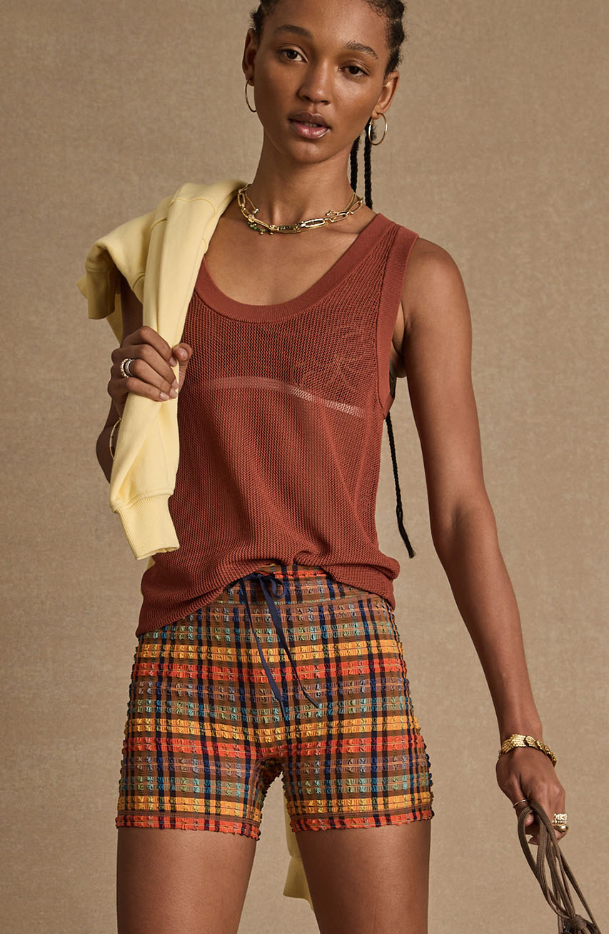 Person wearing a tank top and plaid shorts, holding a yellow sweater.