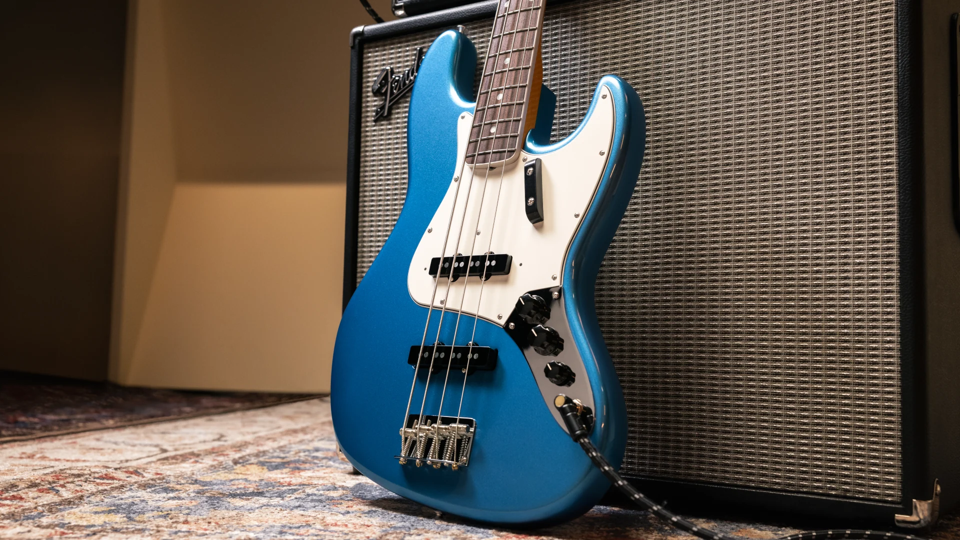 Blue Fender American Vintage II 1966 Jazz Bass leaning against an amplifier on a rug.