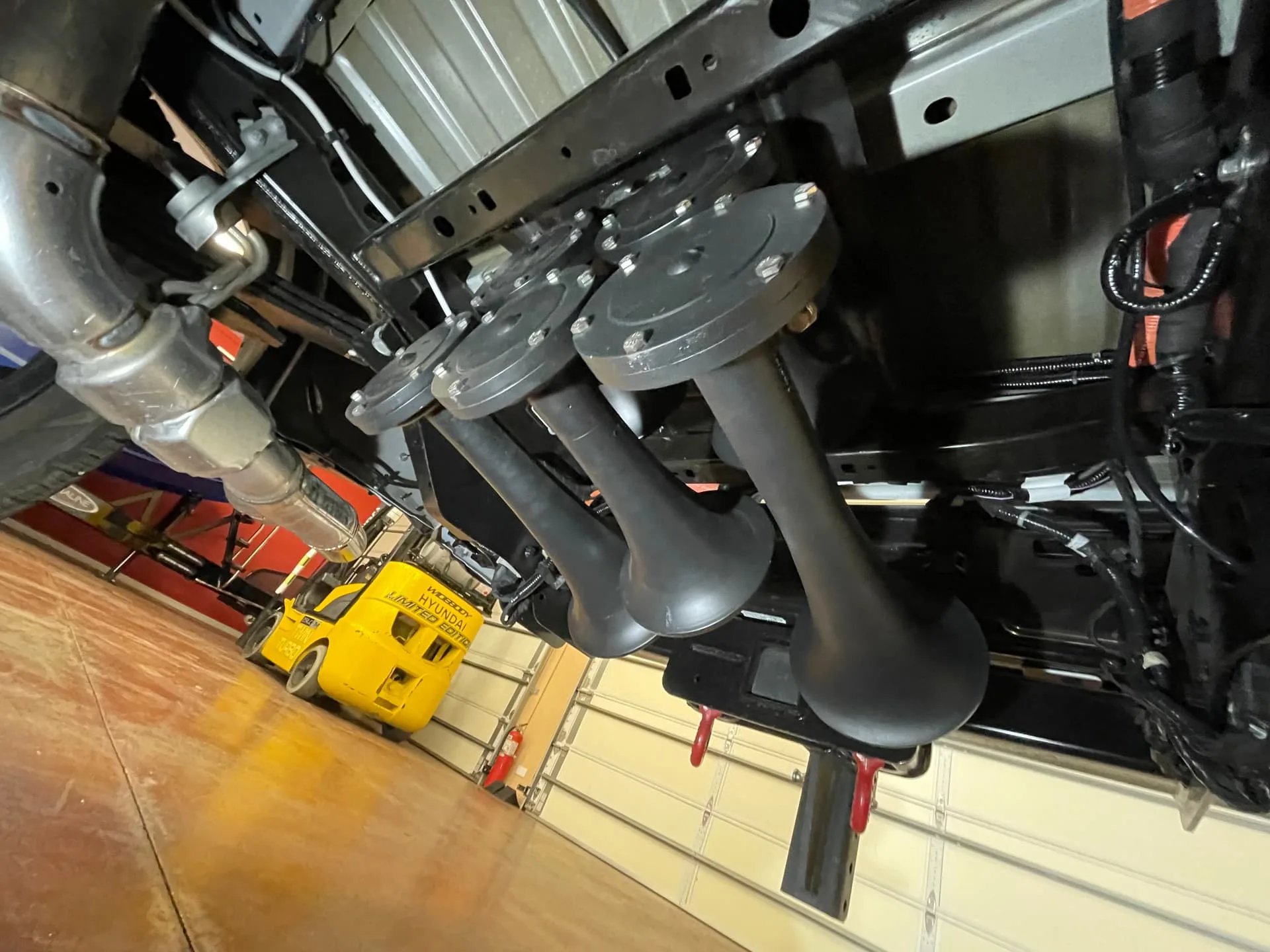 Four matte black train horns mounted on bracket near polished exhaust in garage photo 13