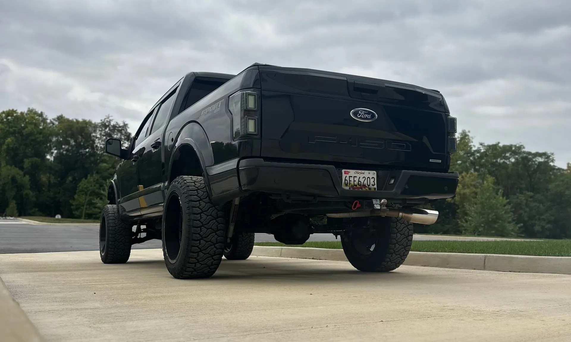 Rear view of Tanner's lifted black Ford F-150 Sport 4x4 with off-road tires parked on concrete