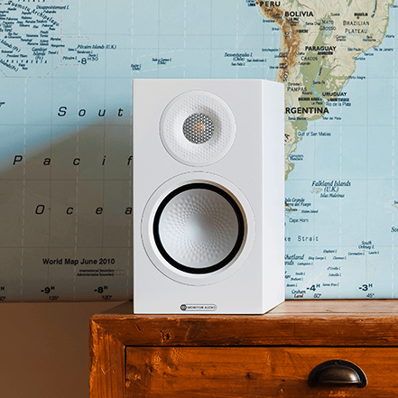 White speaker on a wooden surface in front of a world map.
