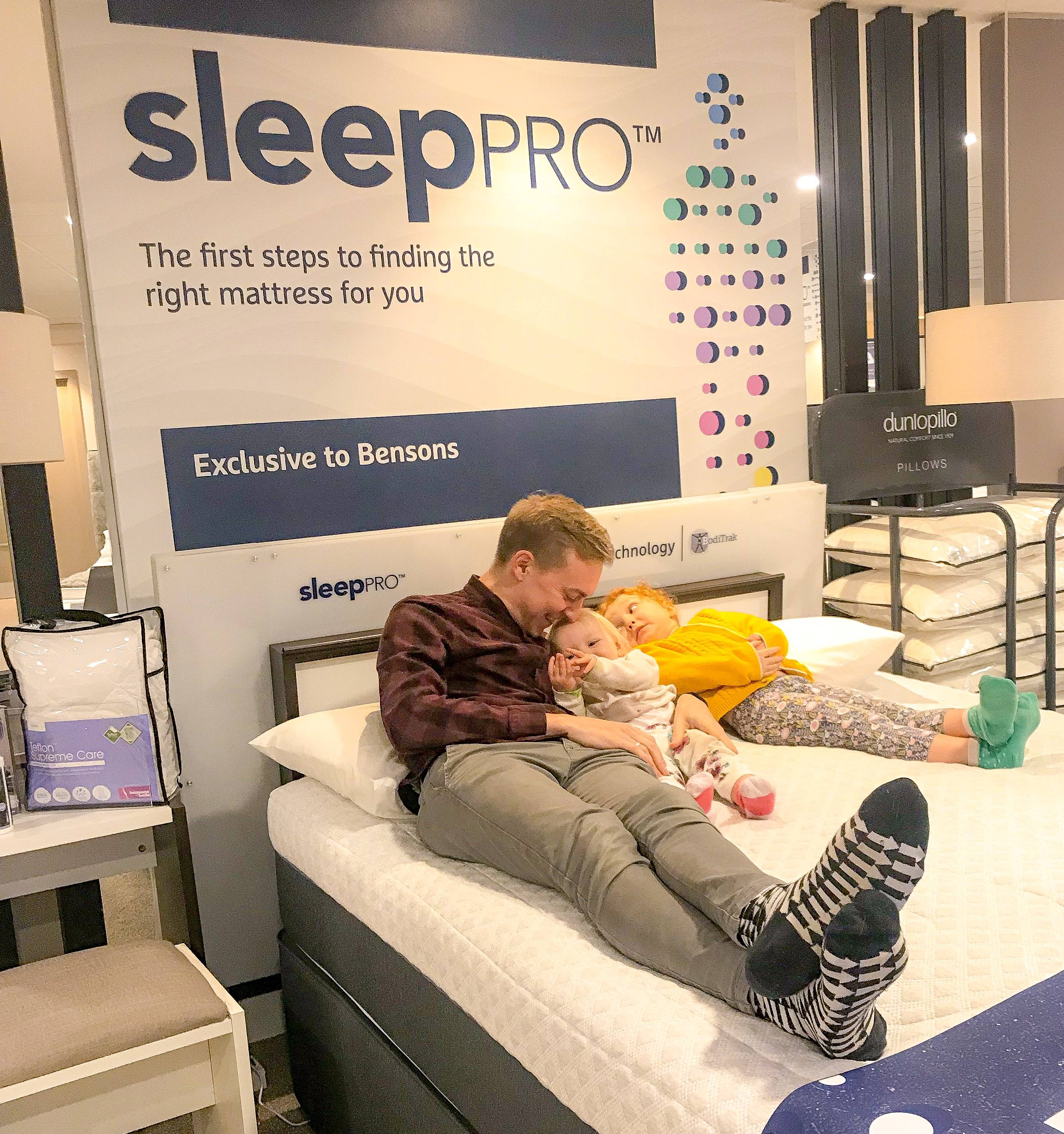 A smiling man cuddles a toddler as he lies next to another child on a SleepPRO bed.