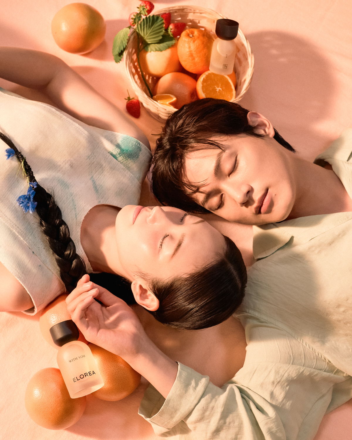 Two people resting with oranges and cosmetic bottles around them.