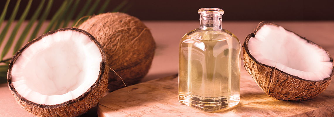 Coconut halves and a bottle of coconut oil on a wooden surface.