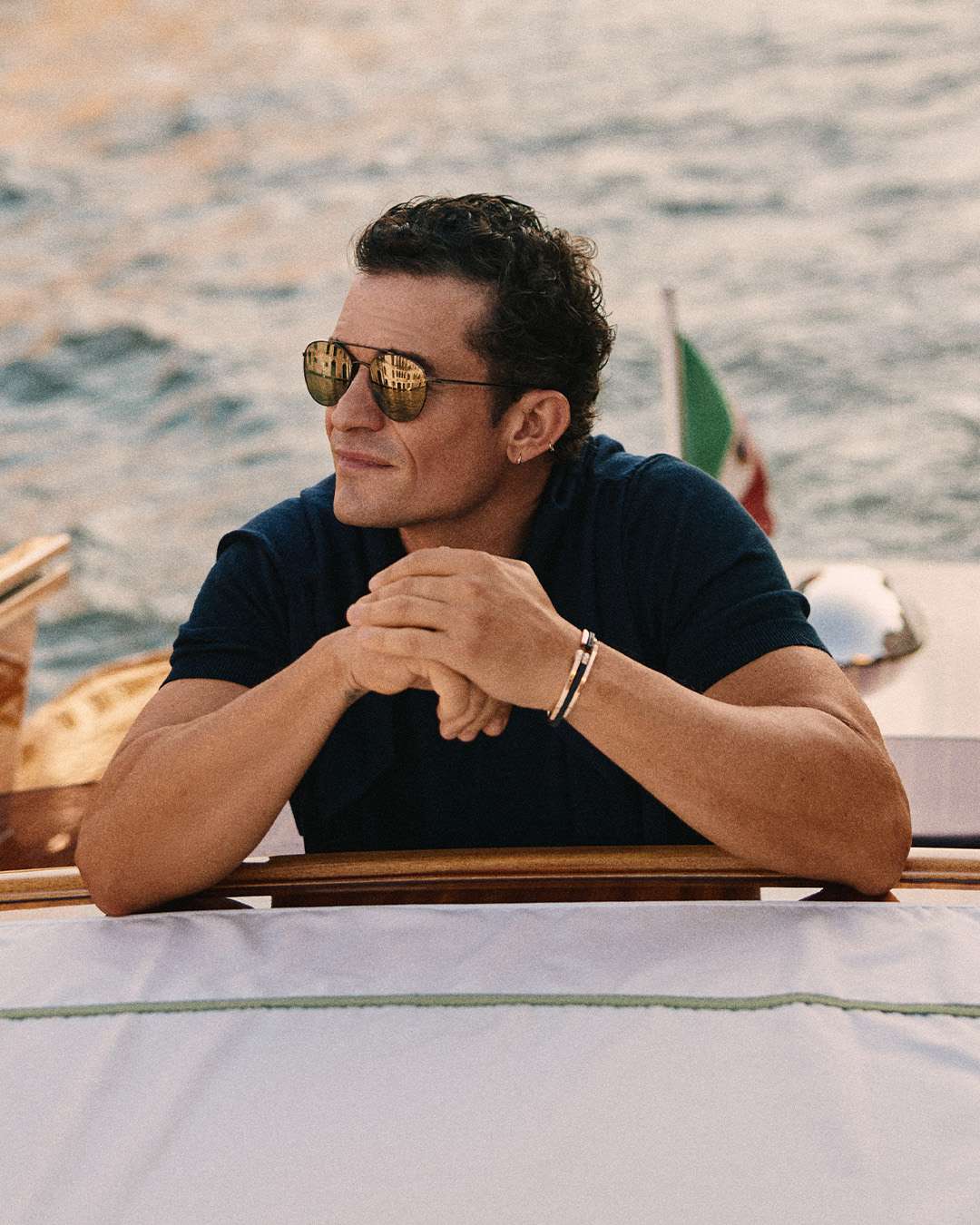 Man with sunglasses leaning on a boat railing by the water.