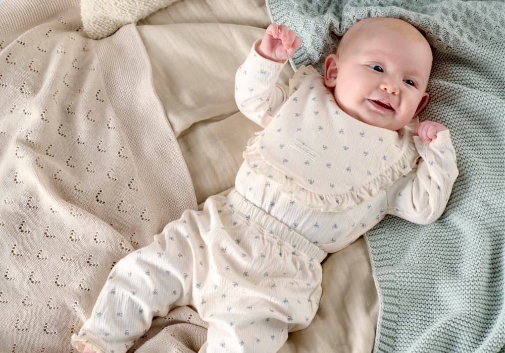 A baby girl lies on a bed of blankets in a matching 3 piece outfit with a ditsy floral print.