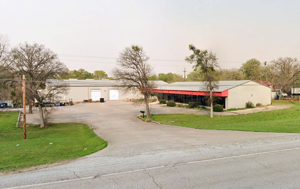 Aerial view of a commercial building with surrounding trees and parking area.