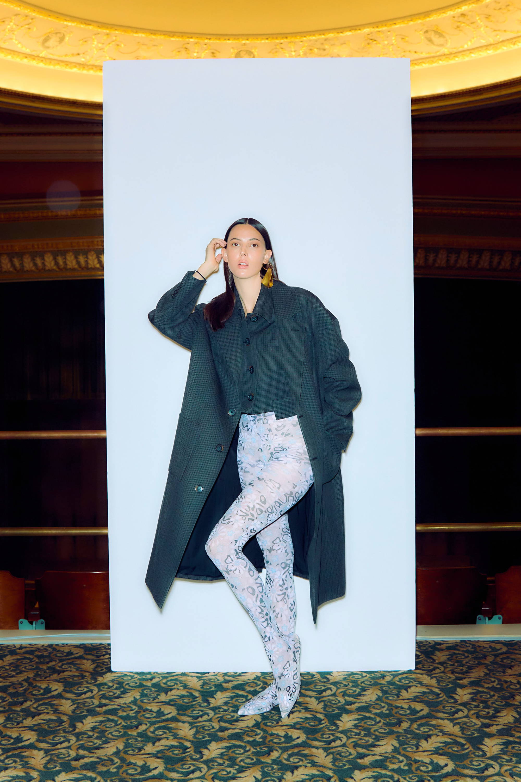 Woman in a black coat and patterned leggings poses against a white backdrop.