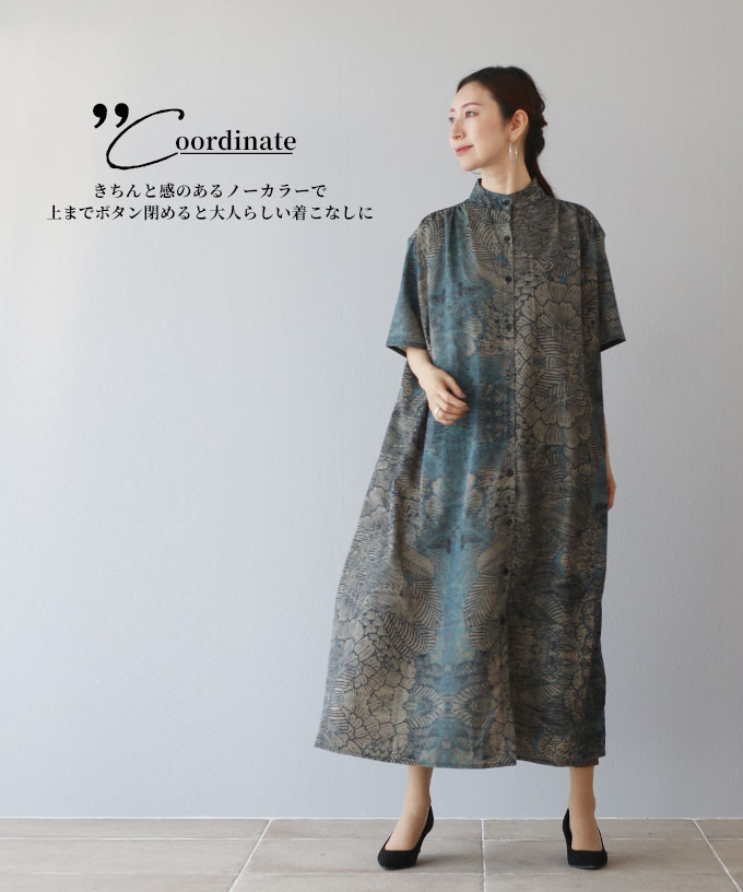 A woman in a patterned dress stands against a neutral background.