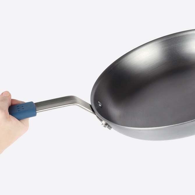 A close view of the Misen Carbon Steel Pan’s durable material, with a hand visible gripping the removable silicone handle grip.