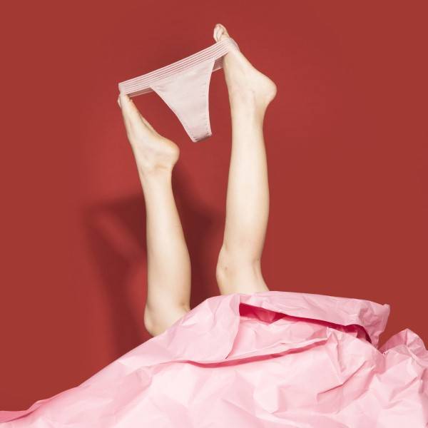 Fotografia da parte inferior de duas pernas segurando uma calcinha absorvente com os pés