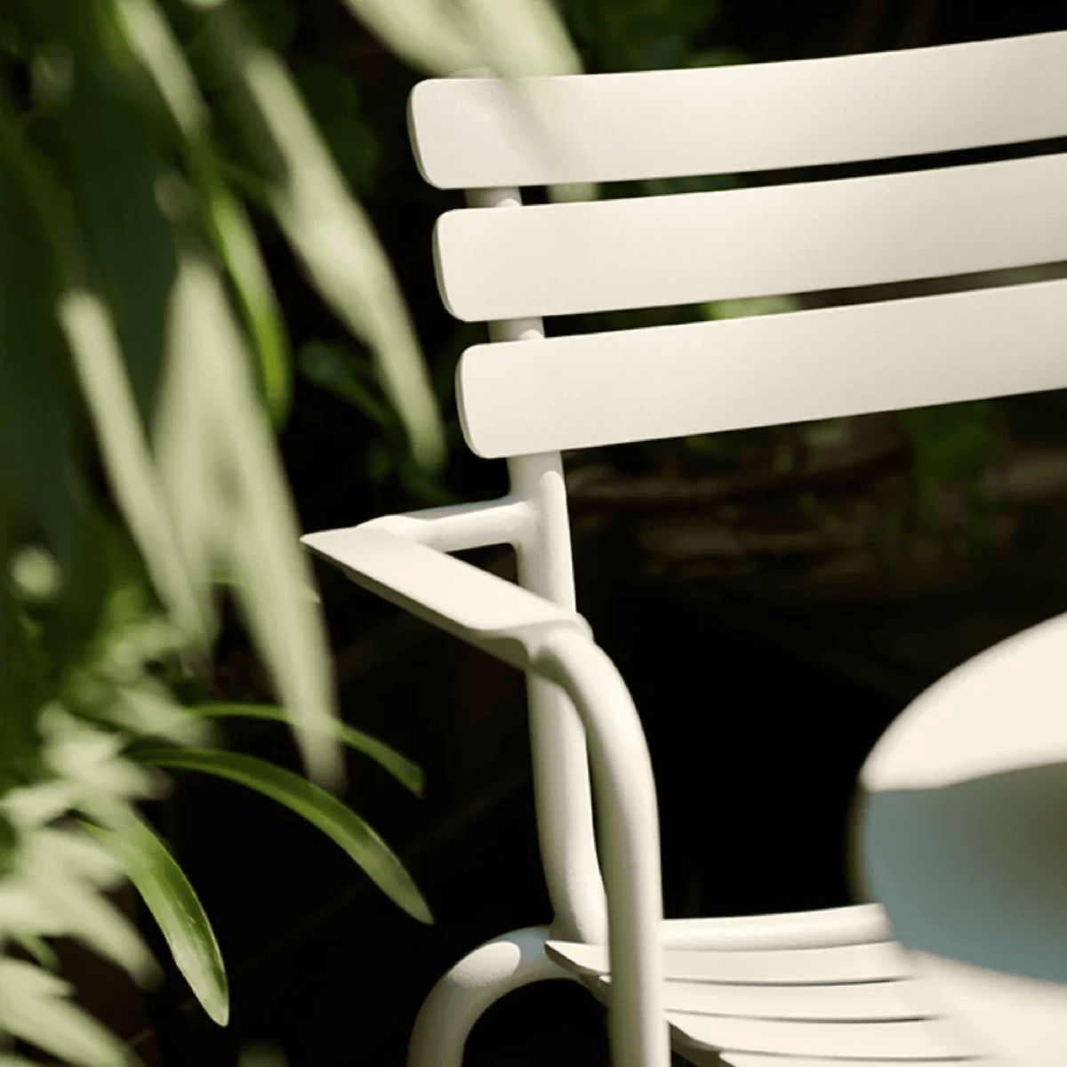 Close-up of powder-coated aluminum outdoor chair with slatted back in a landscaped garden setting