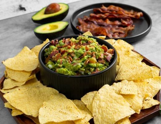 Chips with guacamole and bacon, garnished with avocado halves.