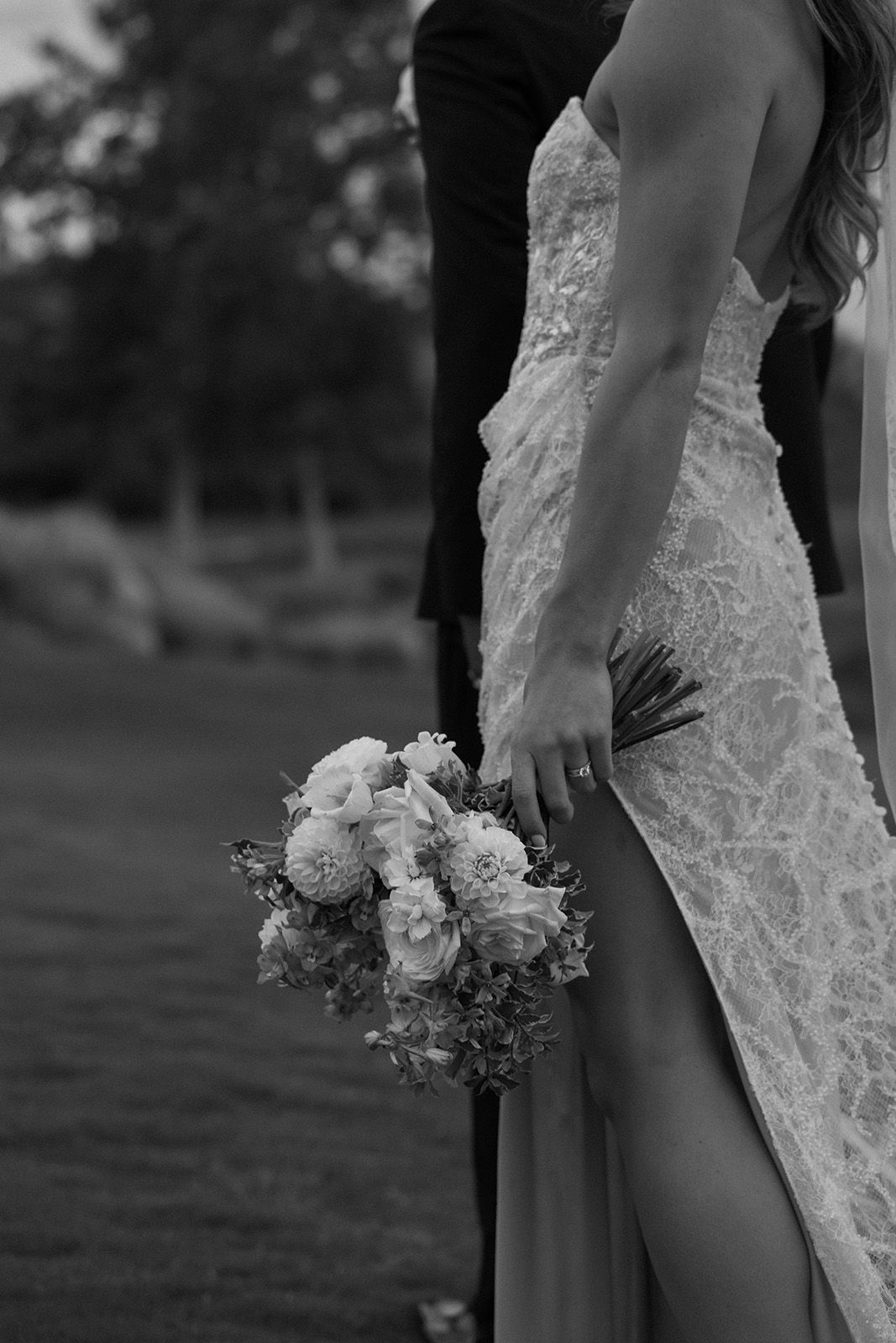 Bride in elegant dress holding bouquet, standing beside a person in formal attire.