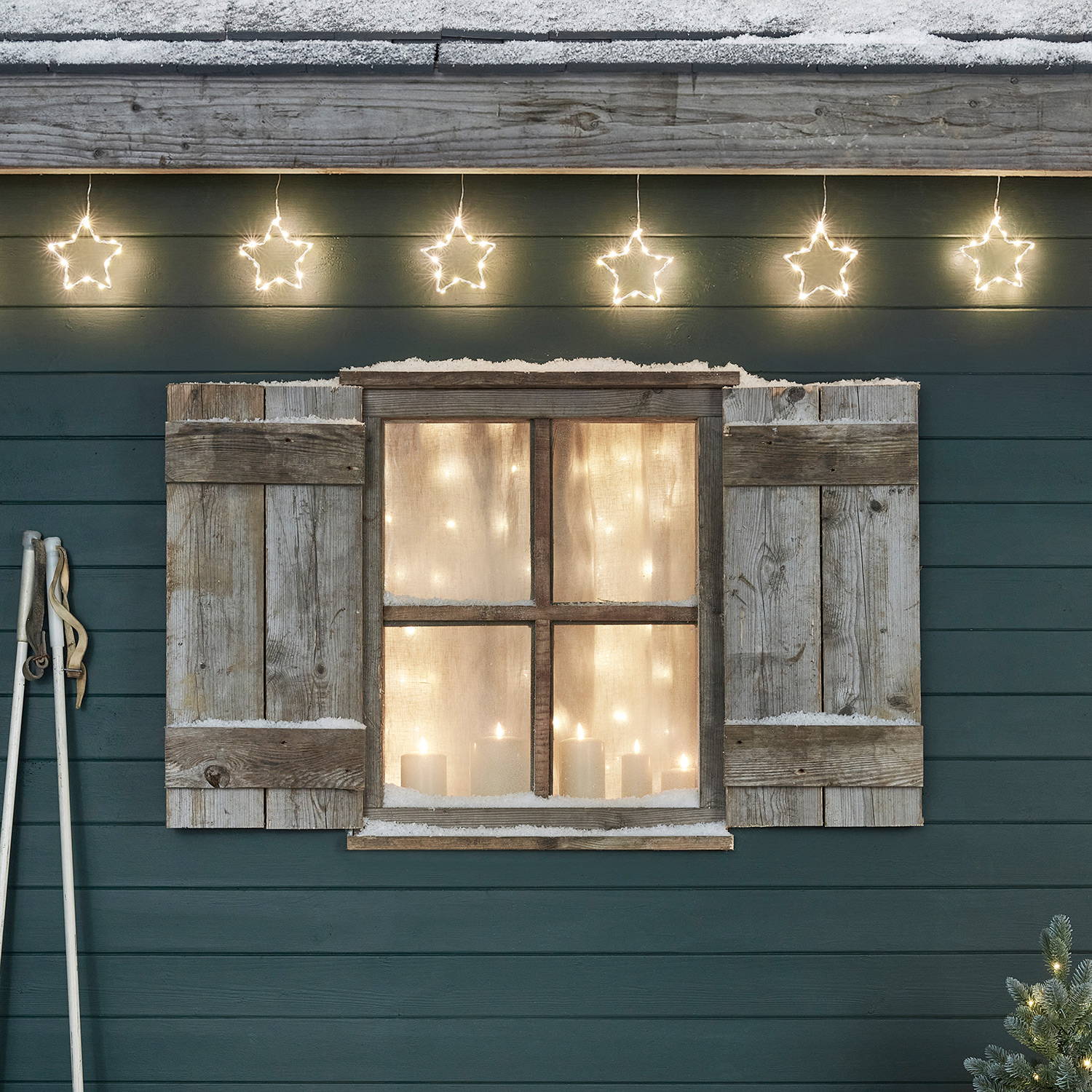 Outdoor view of a window with fairy lights inside and star curtain lights above it.