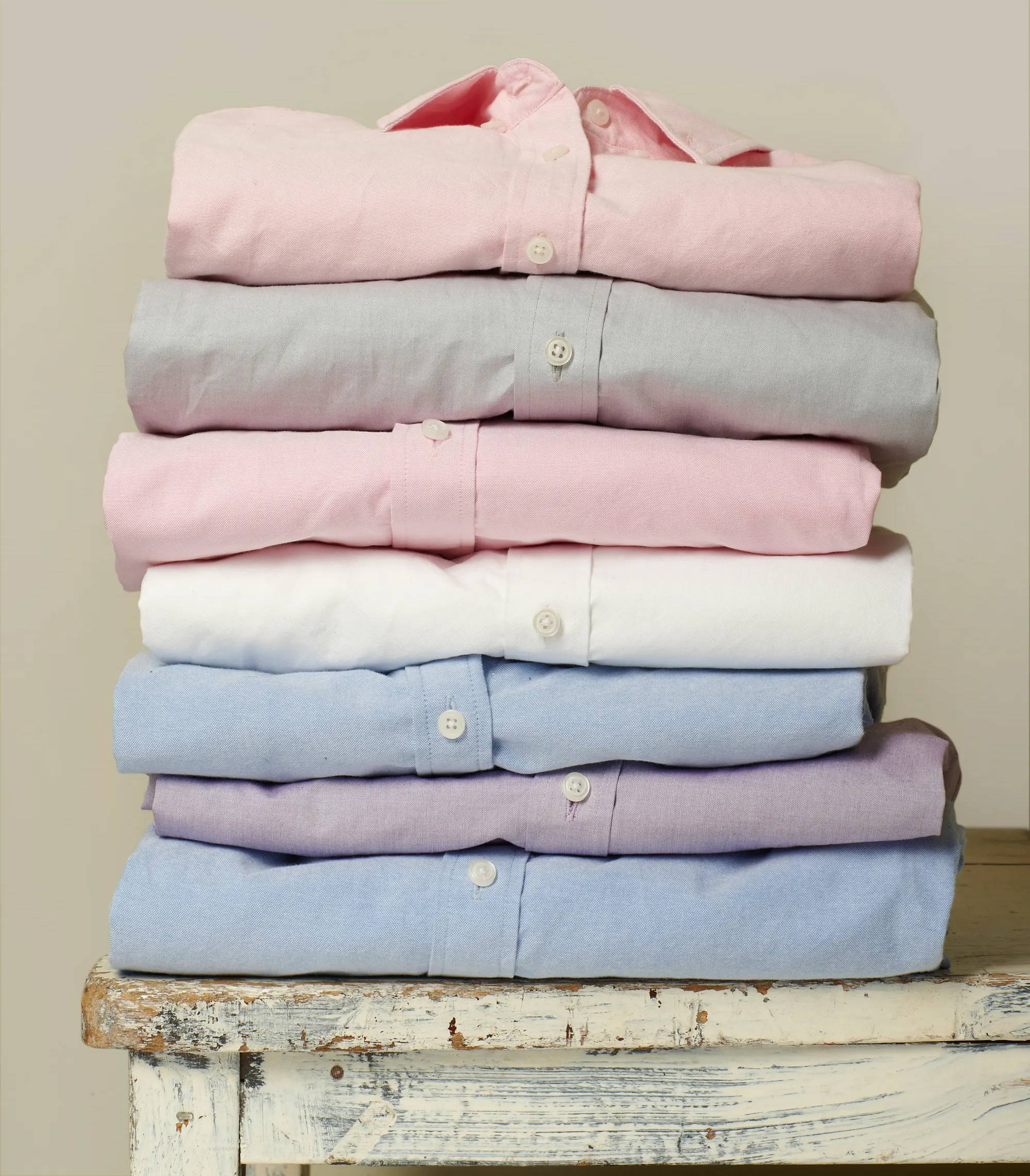 A stack of bespoke dress shirts for men, pink, light grey, light pink, white, light blue, purple