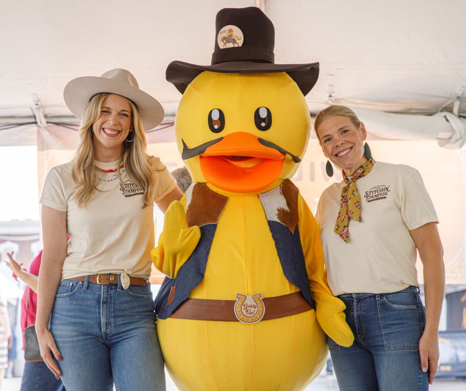 Two women pose with a large cowboy duck mascot.