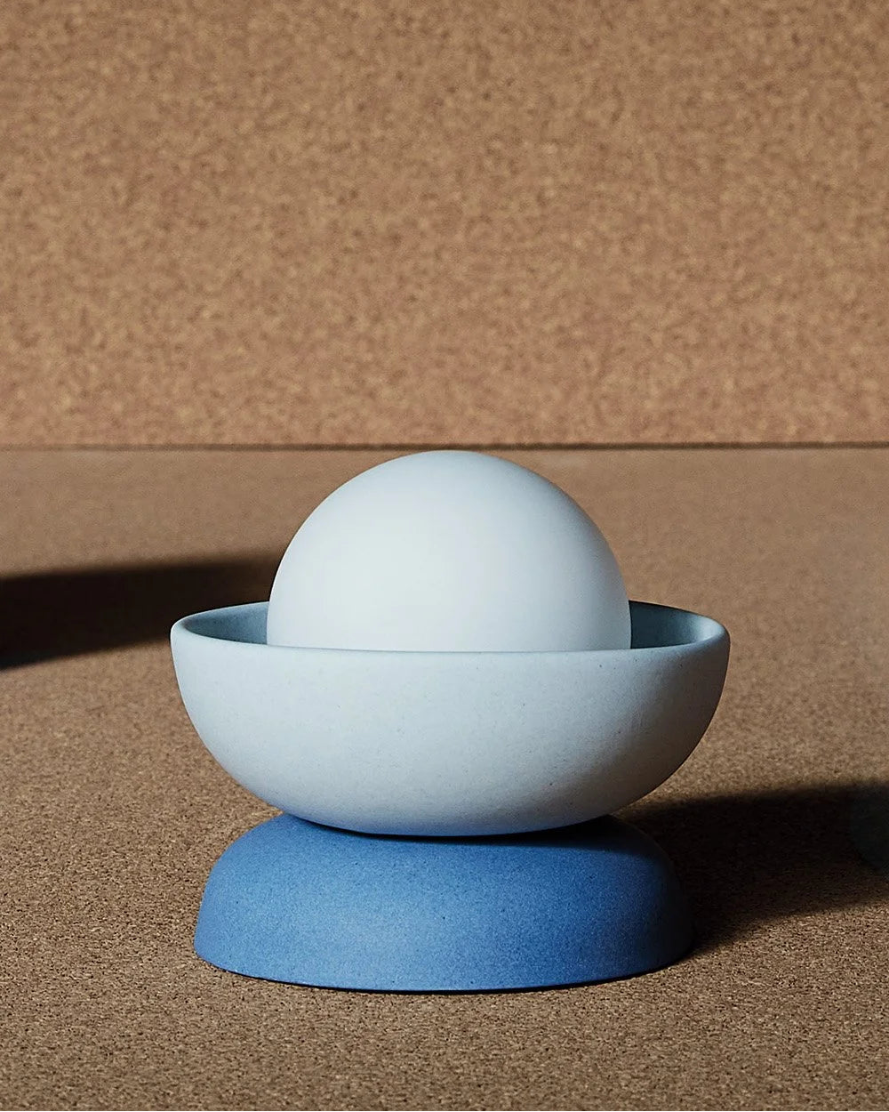 Blue ceramic Studio Enti wall sconce with a white sphere inside on a brown surface