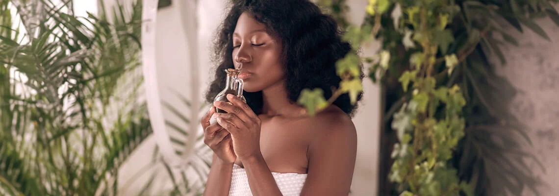 Woman with curly hair holding a bottle, surrounded by greenery.