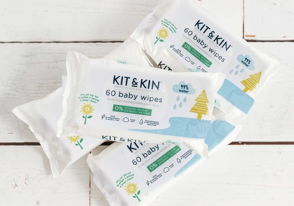 Four packs of Kit and Kin baby wipes are arranged against the backdrop of a white wooden floor.