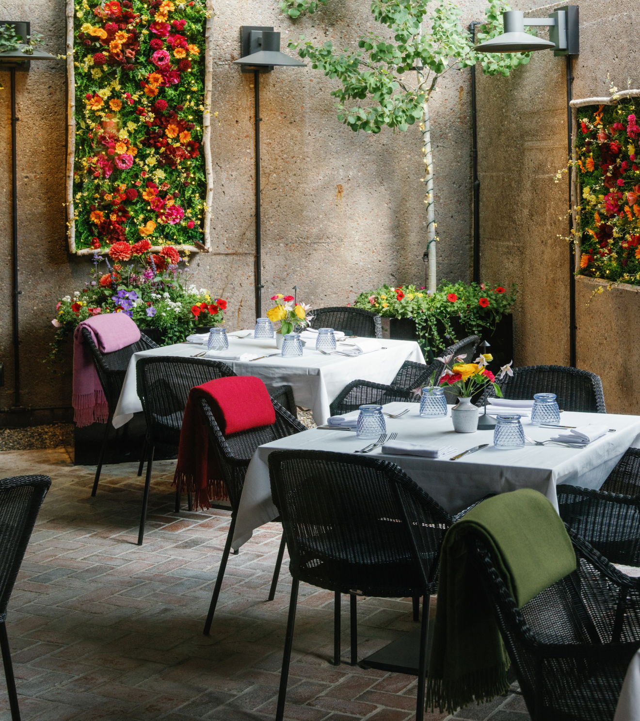 Outdoor restaurant setting with tables, colorful flowers, and greenery.