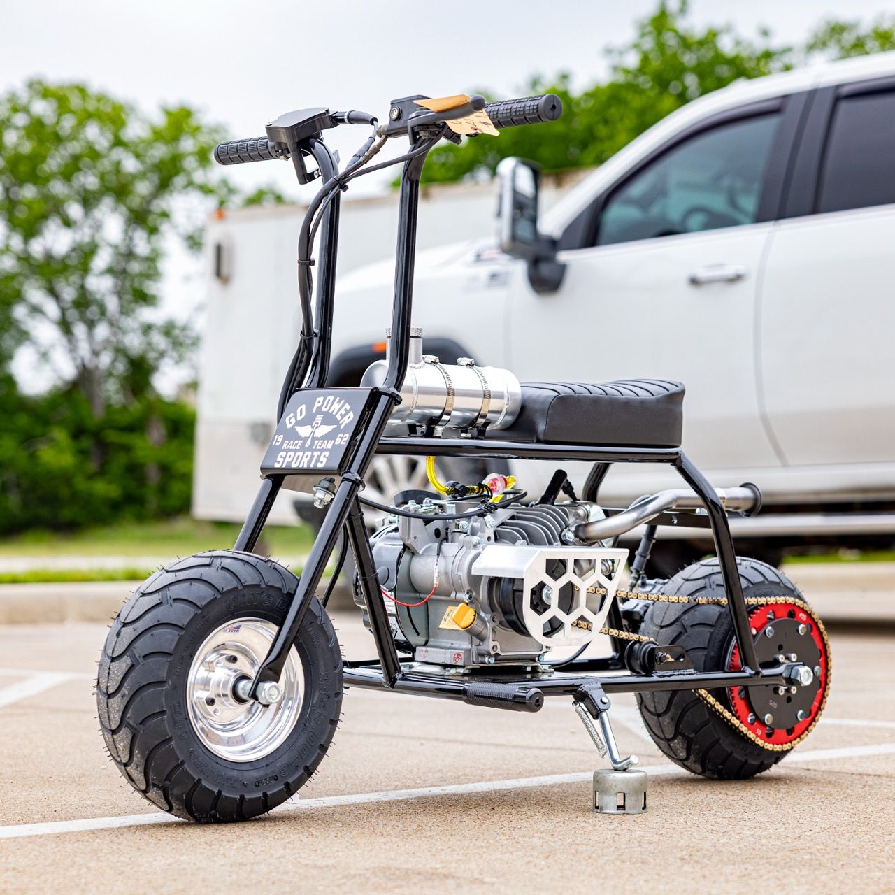 A small black motorbike with large tires parked beside a truck.