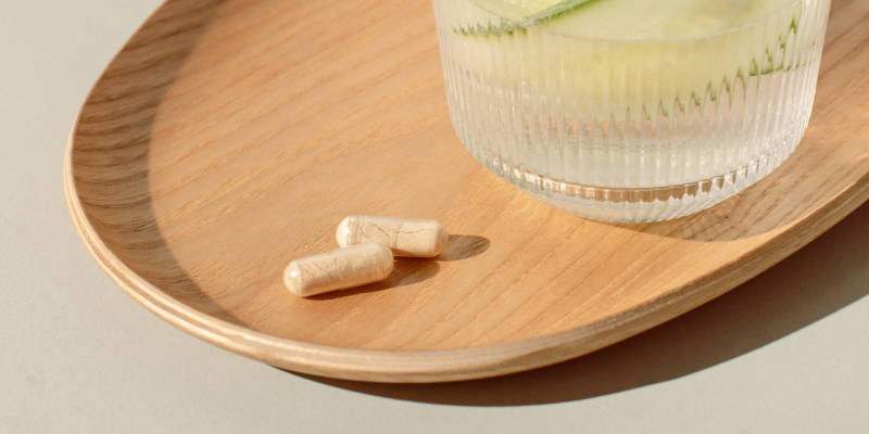 Wasserglas und zwei Kapseln auf einem Tablett