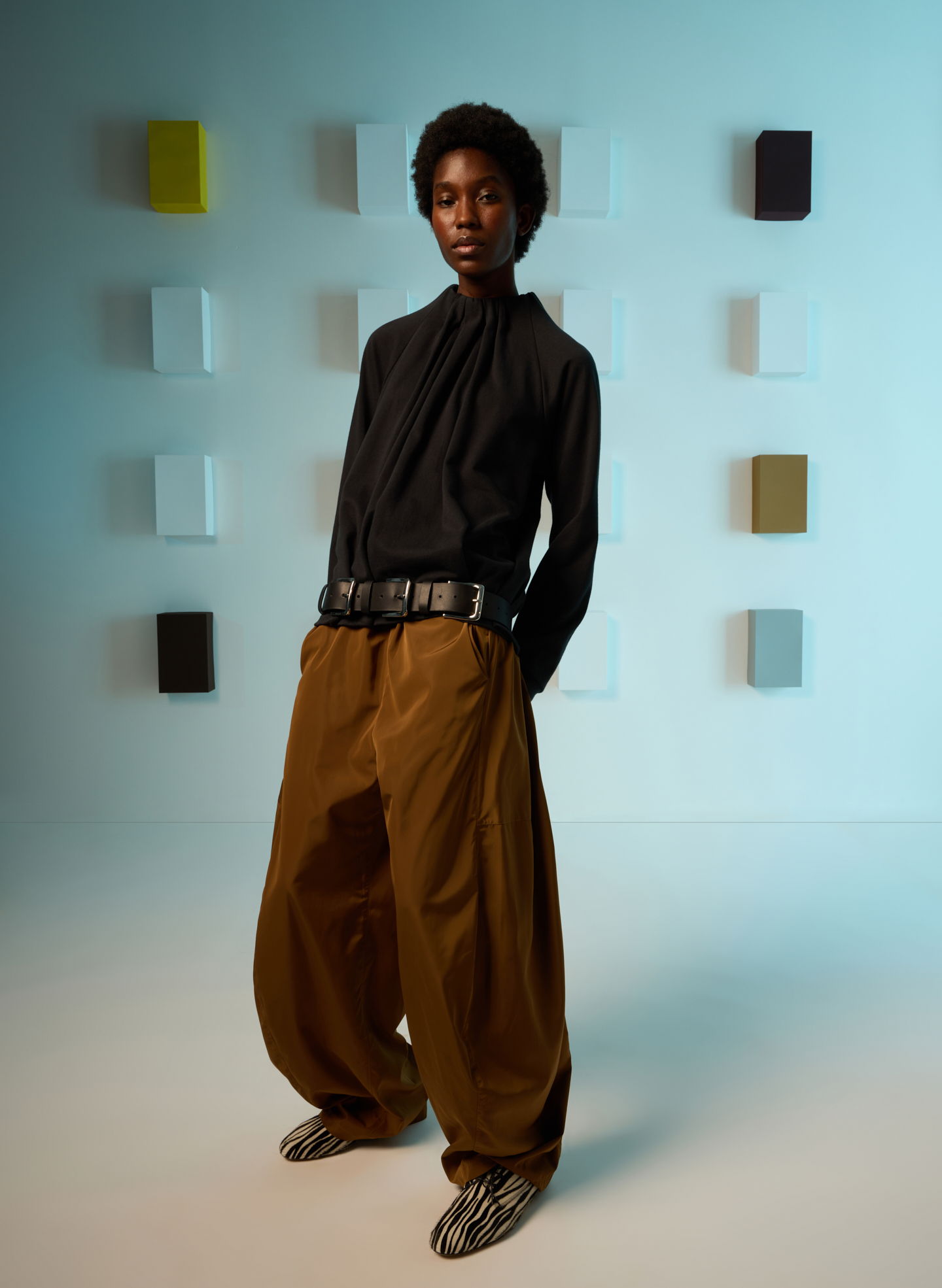 Model in black top and brown pants against a colorful background.