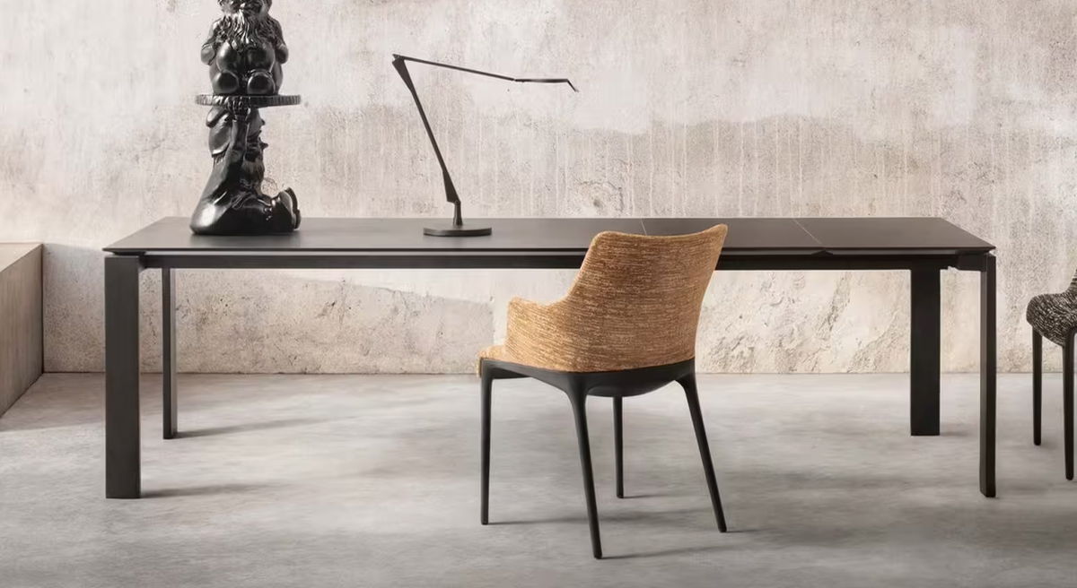 A modern Four Extendable Dining Table by Kartell with a chair and decorative sculpture.