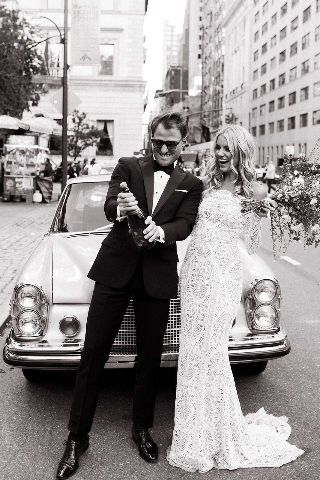Bride and groom leaning on old vintage car and popping chamagne